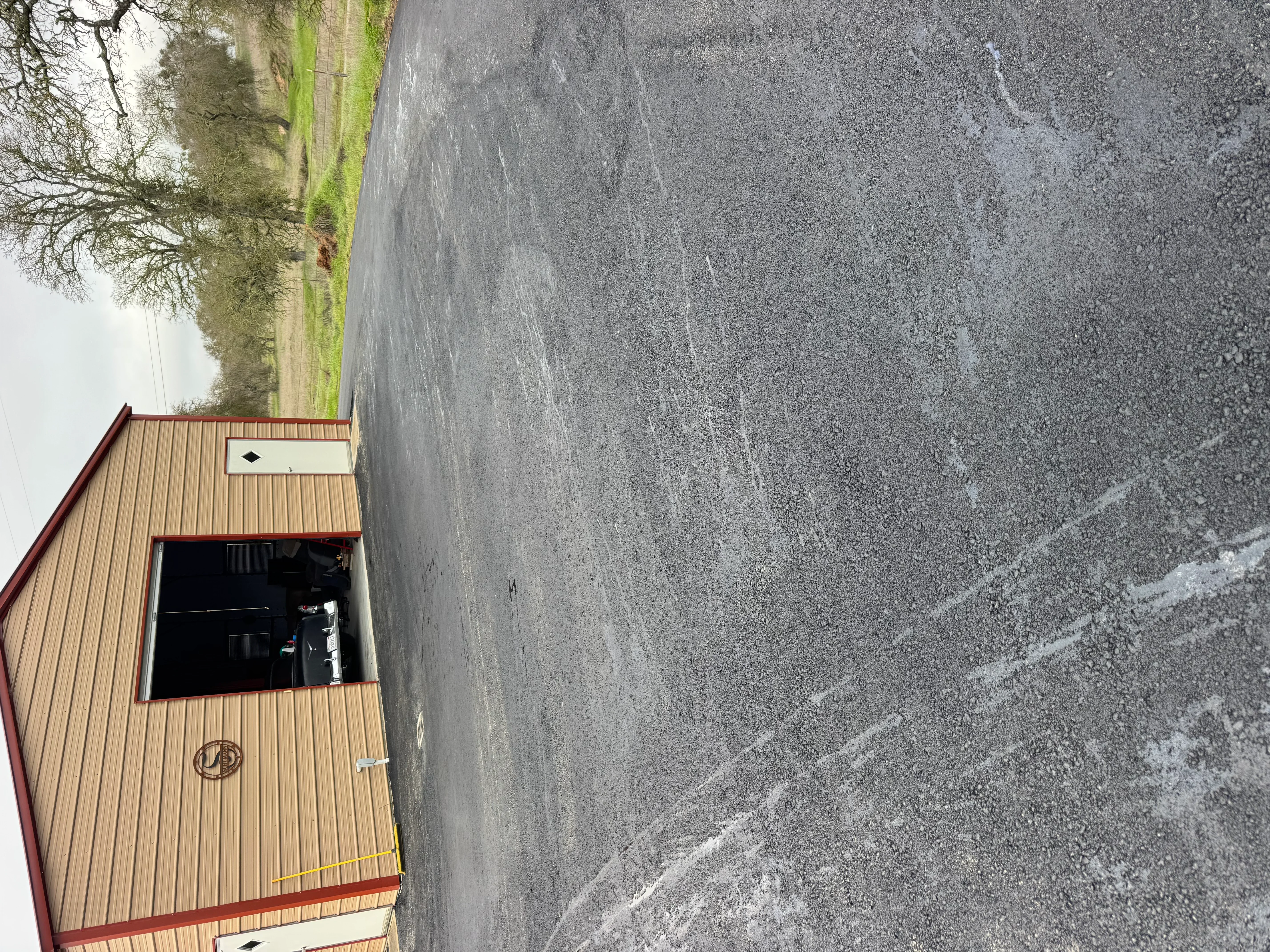 Newly paved asphalt driveway next to commercial building with metal siding