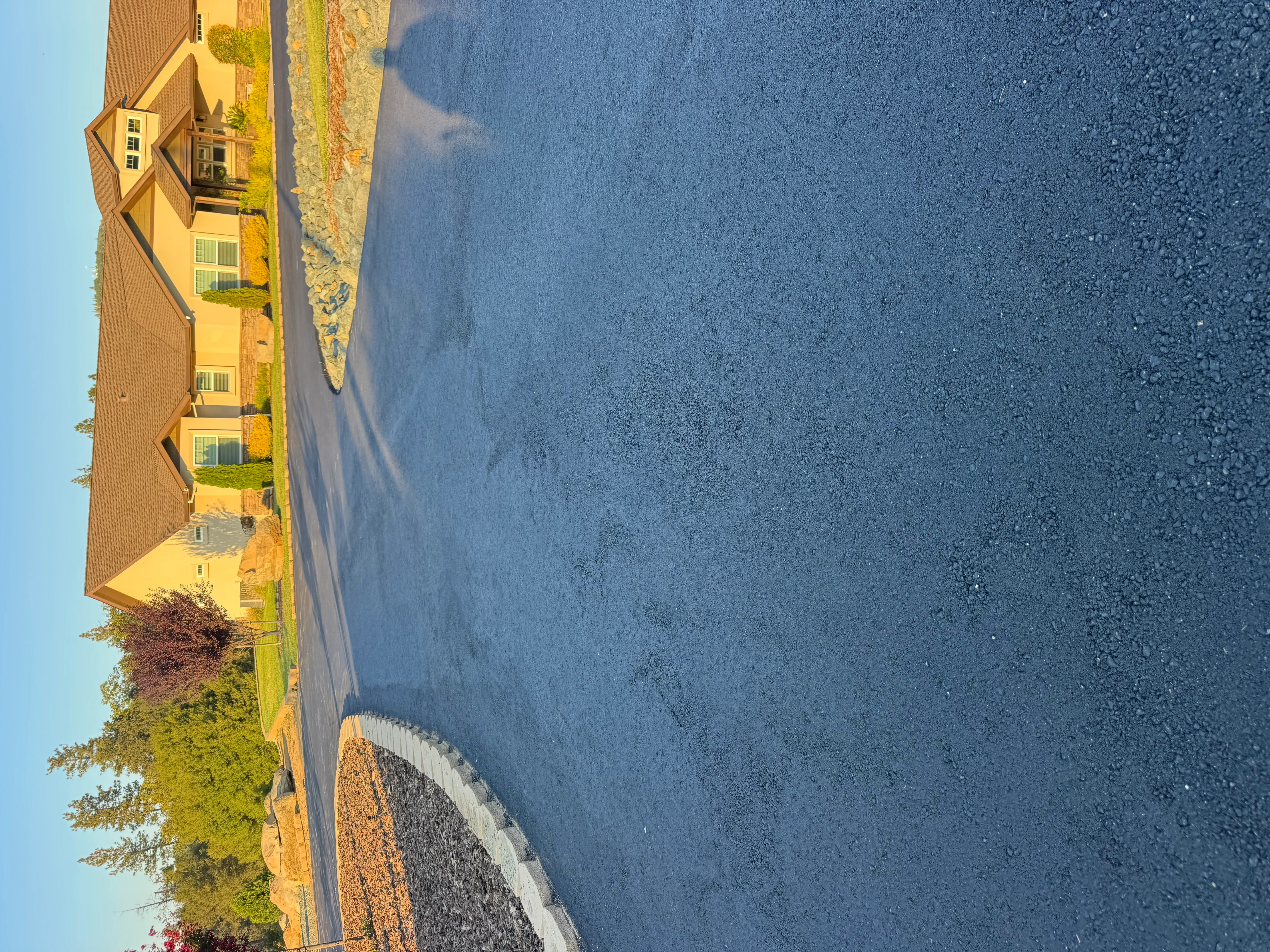 Newly paved residential asphalt driveway with white concrete edge curbing