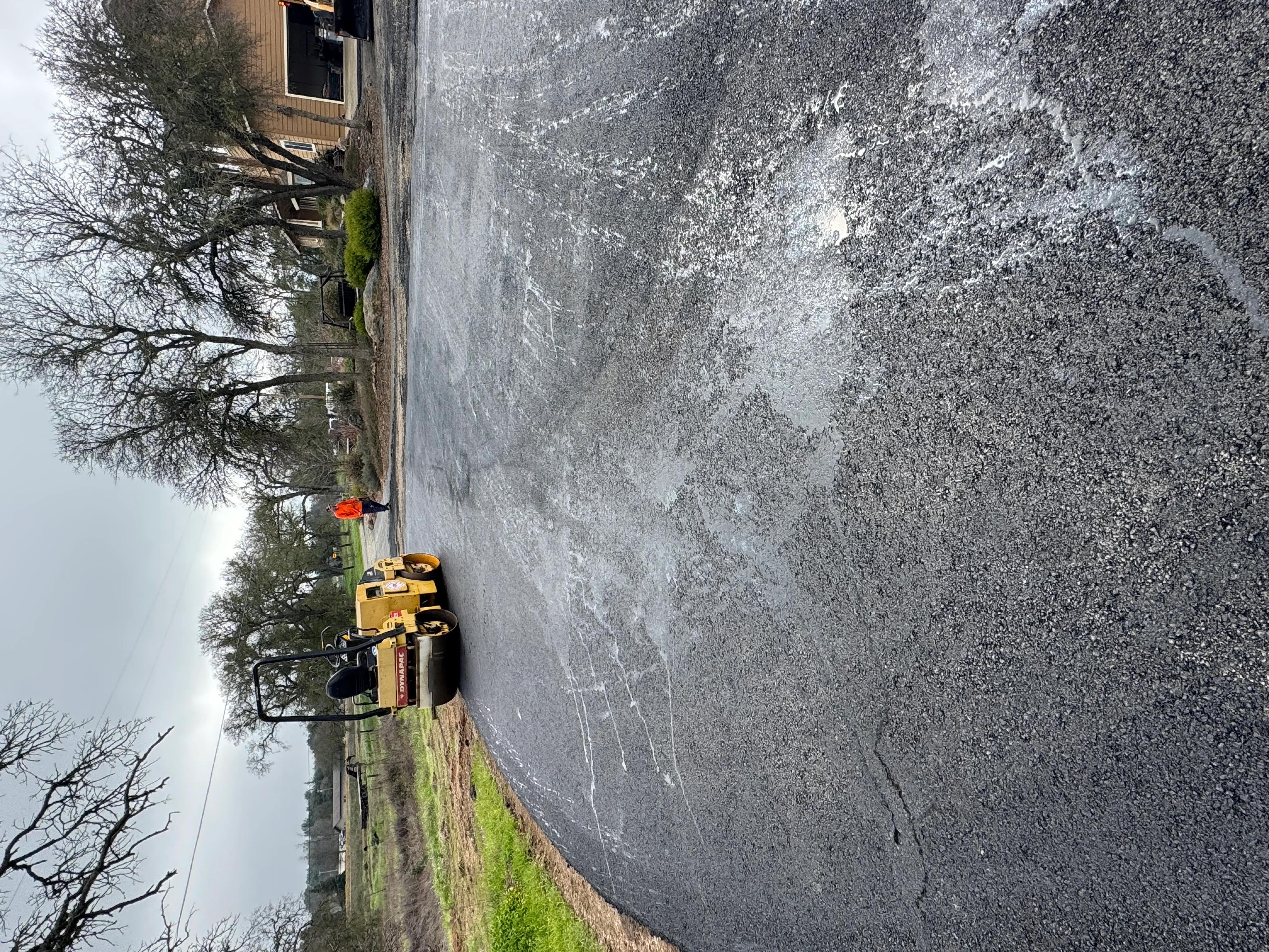 Yellow compactor machine on freshly paved asphalt driveway with residential home in background