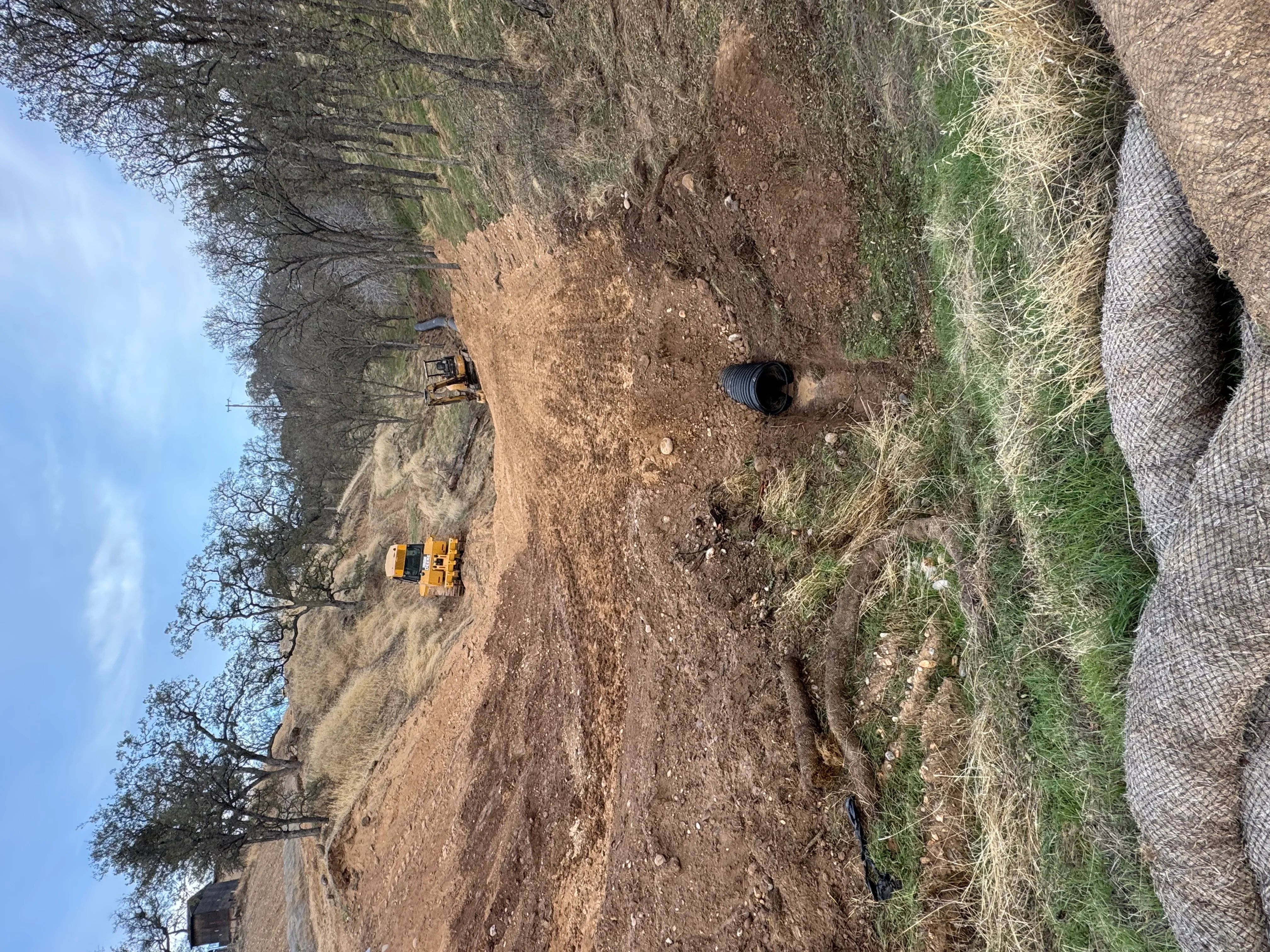 Yellow excavator grading dirt driveway site with erosion control fabric
