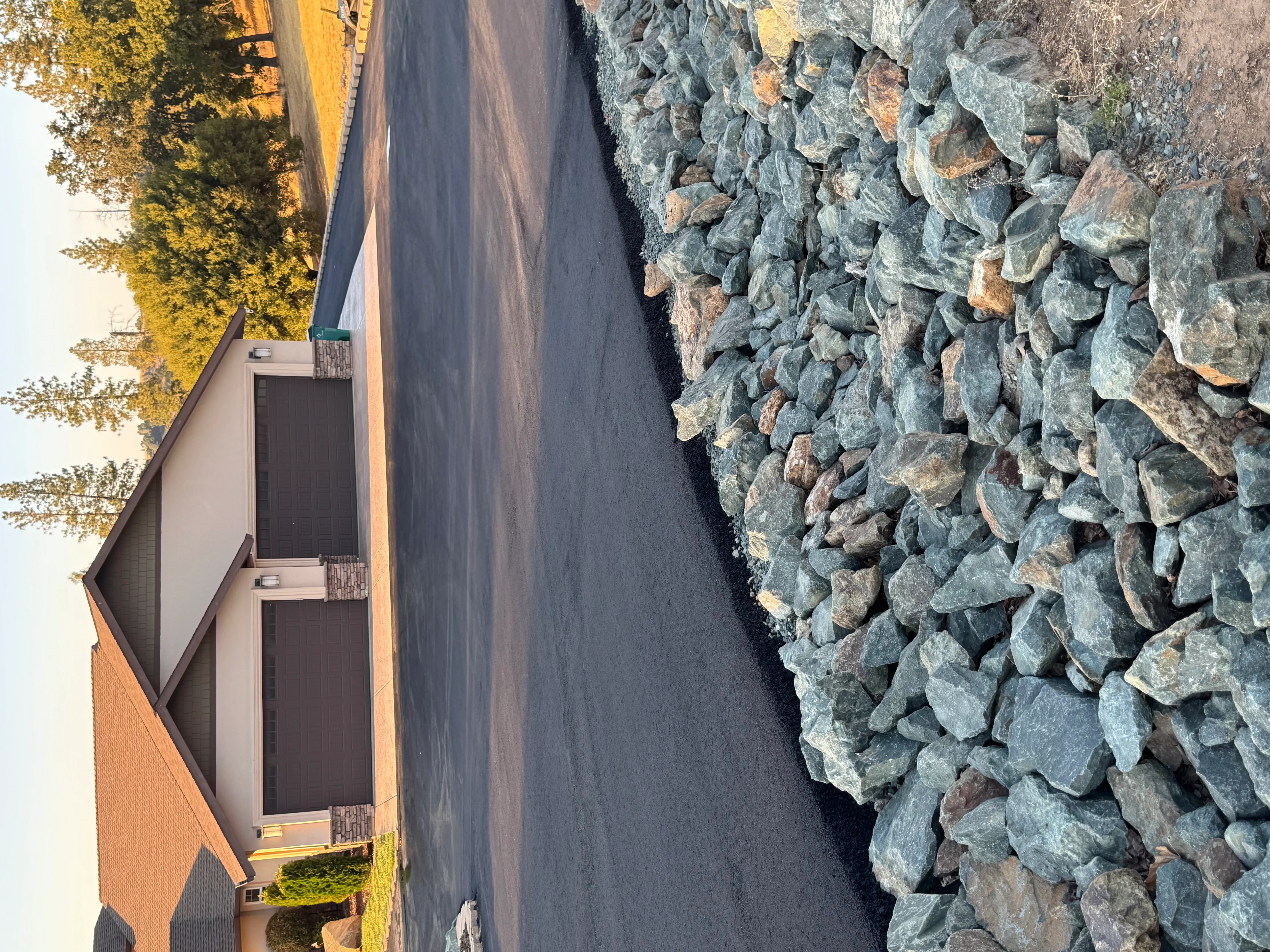 New asphalt driveway with stone border edging alongside brick home