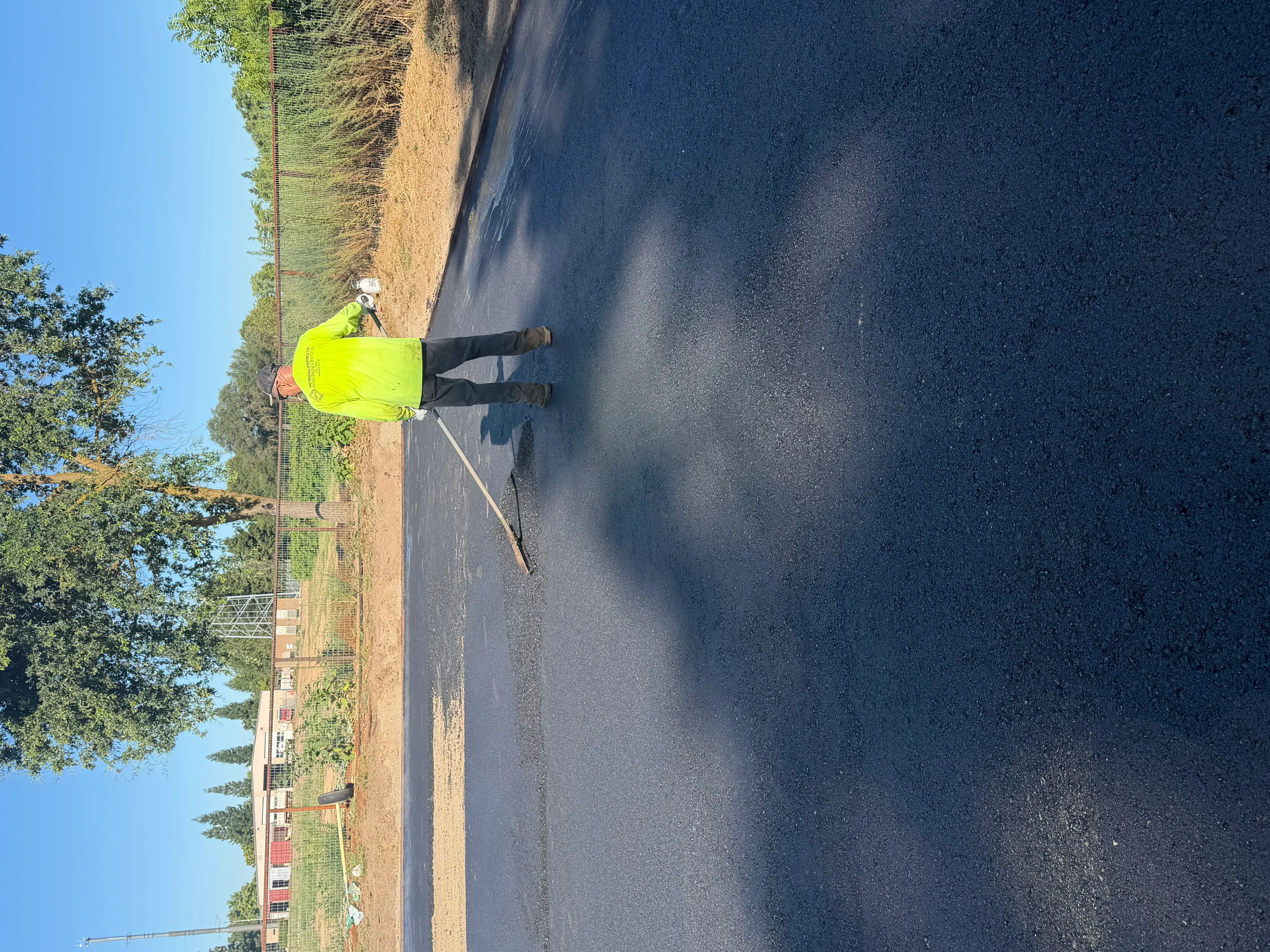 Worker in yellow safety vest inspecting newly paved dark asphalt driveway